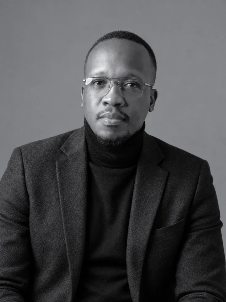 Chakra in a dark blazer and roll-neck, seated in the studio